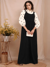 Elegant model wearing a modest black and white pinafore over a patterned blouse, styled with accessories